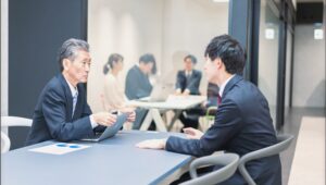 上司と若手社員が落ち着いた雰囲気の中で対話している職場風景